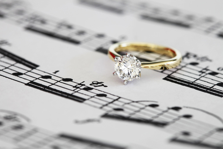 Gold diamond engagement ring resting on a sheet of romantic music notes, symbolizing the harmony of love and proposals.