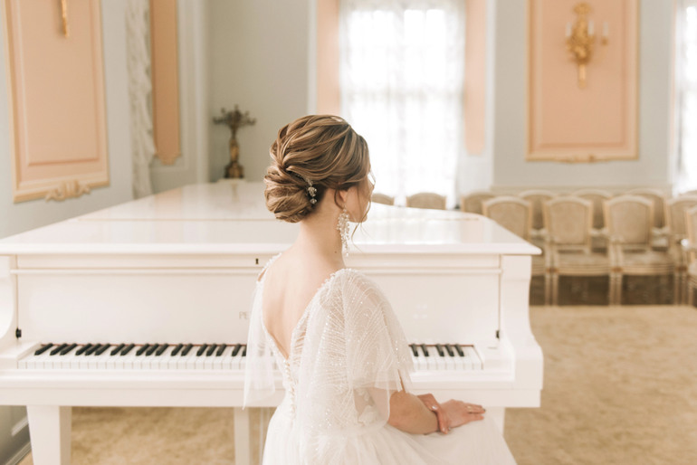 Elegant foreign bride sitting at a white grand piano in a classical room