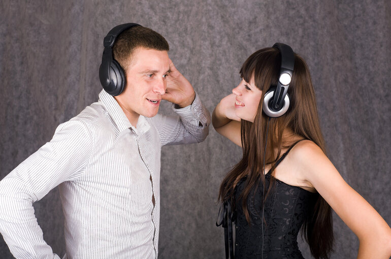 A man and woman wearing headphones facing each other, smiling as they share music together, suggesting chemistry and connection.